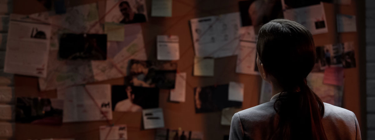 Image of a woman viewing a large investigation board with many photos, notes and documents pinned to it